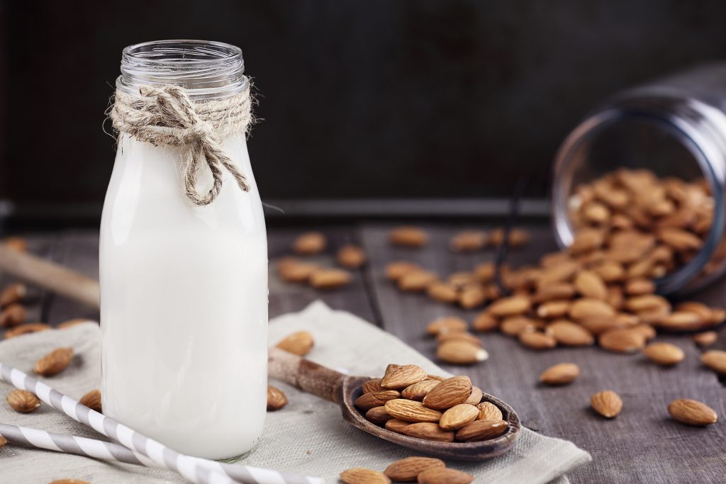 Organic white almond milk in a glass bottle with whole almonds spilled over a rustic wooden table. Organic white almond milk in a glass bottle with whole almonds spilled over a rustic wooden table.