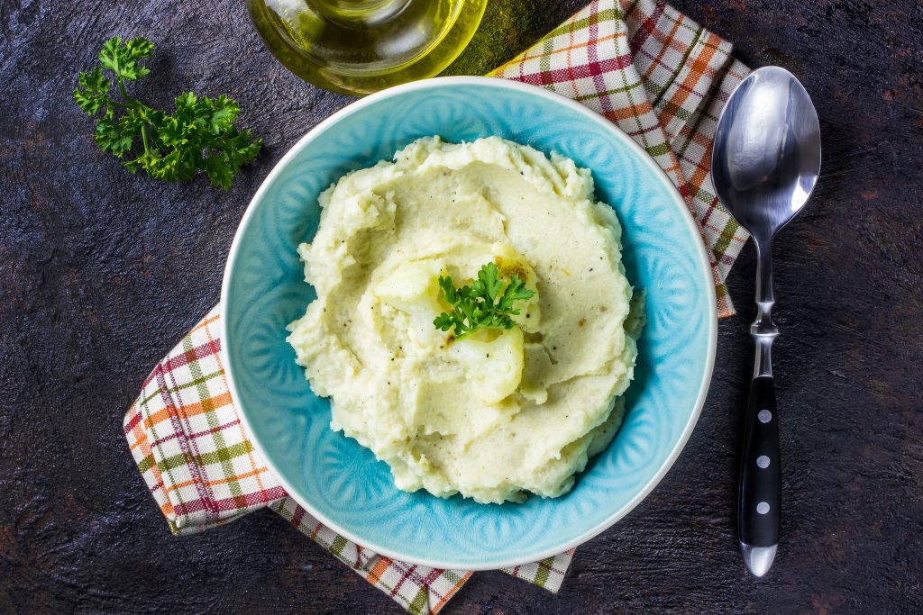 Mashed cauliflower with oil in blue bowl on wooden table. Mashed cauliflower with oil in blue bowl on wooden table. Dinner for a low-carb, keto diet